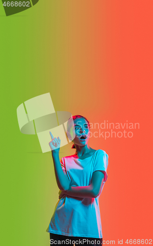 Image of Young caucasian girl\'s portrait on gradient green-orange studio background in neon light