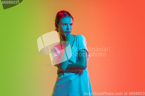 Image of Young caucasian girl\'s portrait on gradient green-orange studio background in neon light