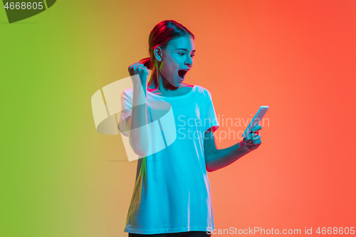 Image of Young caucasian girl\'s portrait on gradient green-orange studio background in neon light