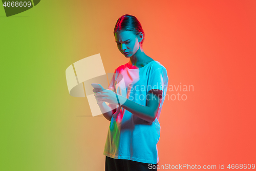 Image of Young caucasian girl\'s portrait on gradient green-orange studio background in neon light