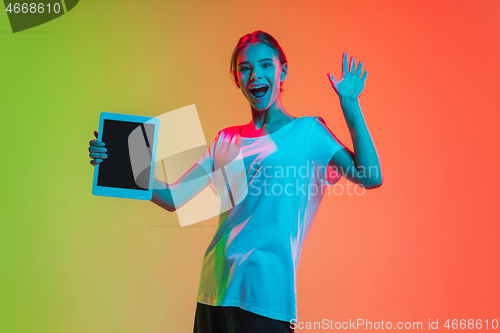 Image of Young caucasian girl\'s portrait on gradient green-orange studio background in neon light