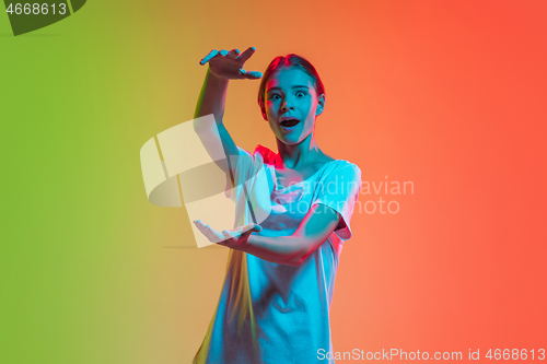 Image of Young caucasian girl\'s portrait on gradient green-orange studio background in neon light