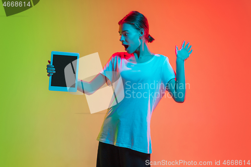Image of Young caucasian girl\'s portrait on gradient green-orange studio background in neon light