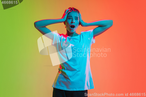 Image of Young caucasian girl\'s portrait on gradient green-orange studio background in neon light