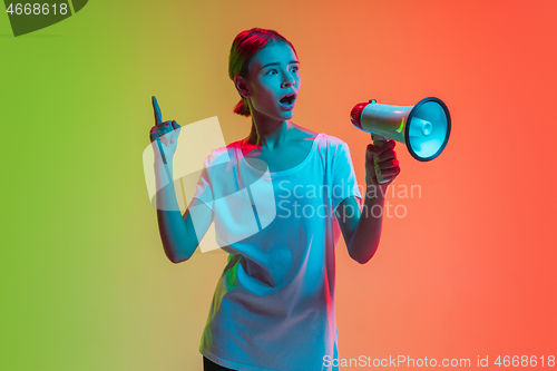 Image of Young caucasian girl\'s portrait on gradient green-orange studio background in neon light