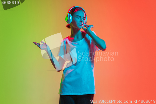 Image of Young caucasian girl\'s portrait on gradient green-orange studio background in neon light