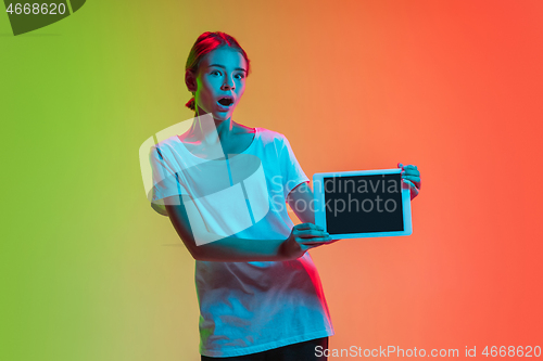 Image of Young caucasian girl\'s portrait on gradient green-orange studio background in neon light