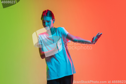 Image of Young caucasian girl\'s portrait on gradient green-orange studio background in neon light