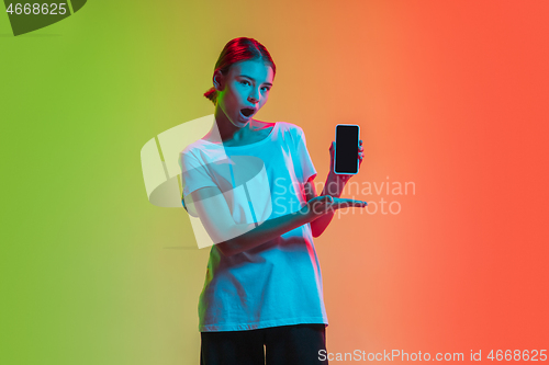 Image of Young caucasian girl\'s portrait on gradient green-orange studio background in neon light