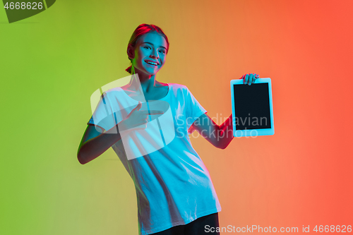 Image of Young caucasian girl\'s portrait on gradient green-orange studio background in neon light