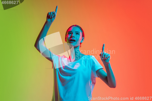 Image of Young caucasian girl\'s portrait on gradient green-orange studio background in neon light