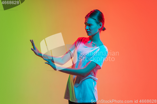 Image of Young caucasian girl\'s portrait on gradient green-orange studio background in neon light