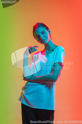 Image of Young caucasian girl\'s portrait on gradient green-orange studio background in neon light