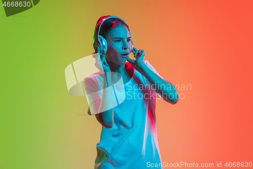 Image of Young caucasian girl\'s portrait on gradient green-orange studio background in neon light