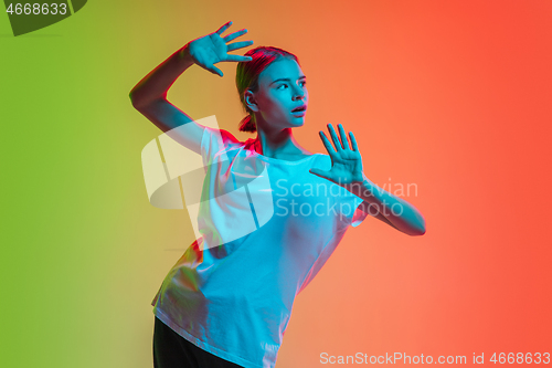 Image of Young caucasian girl\'s portrait on gradient green-orange studio background in neon light