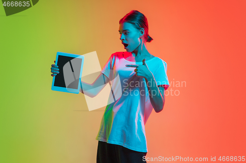 Image of Young caucasian girl\'s portrait on gradient green-orange studio background in neon light