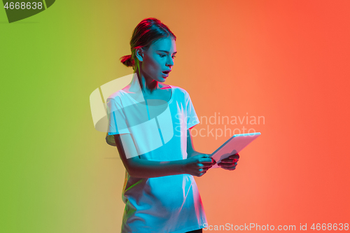 Image of Young caucasian girl\'s portrait on gradient green-orange studio background in neon light
