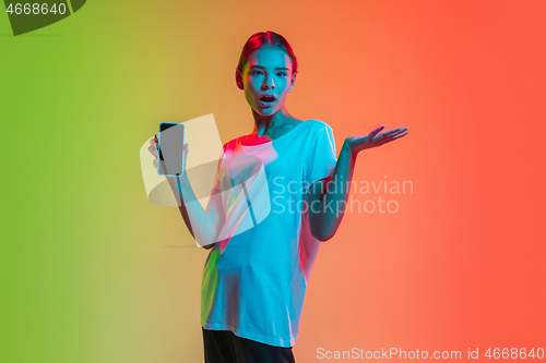 Image of Young caucasian girl\'s portrait on gradient green-orange studio background in neon light