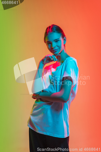 Image of Young caucasian girl\'s portrait on gradient green-orange studio background in neon light