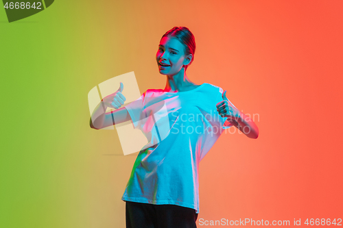 Image of Young caucasian girl\'s portrait on gradient green-orange studio background in neon light