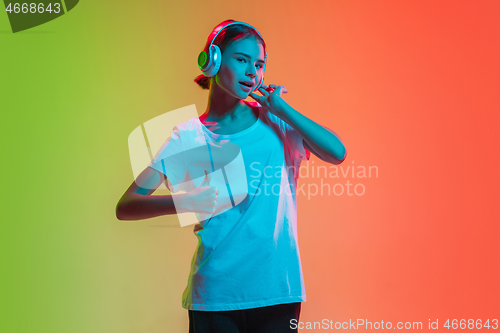 Image of Young caucasian girl\'s portrait on gradient green-orange studio background in neon light