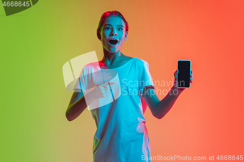 Image of Young caucasian girl\'s portrait on gradient green-orange studio background in neon light