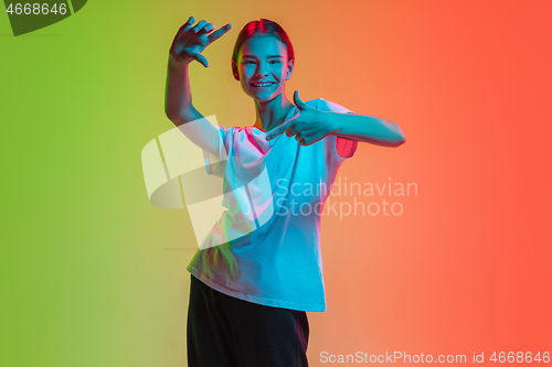 Image of Young caucasian girl\'s portrait on gradient green-orange studio background in neon light