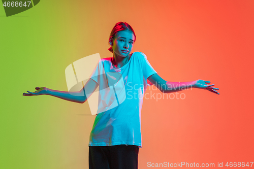 Image of Young caucasian girl\'s portrait on gradient green-orange studio background in neon light