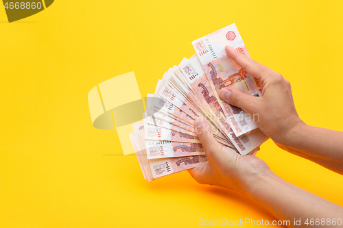 Image of Hands count money in a bundle of notes, yellow background