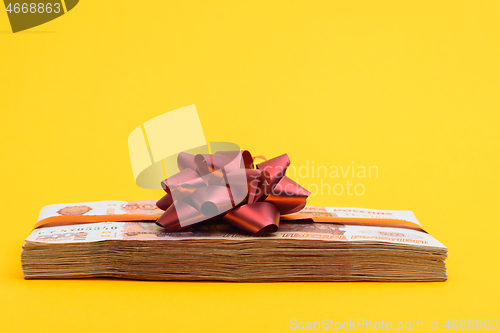 Image of A bundle of money tied with ribbons and bow on a yellow background