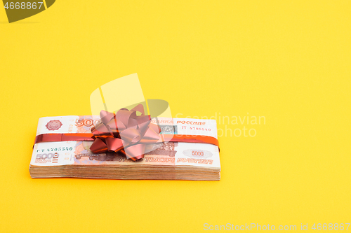 Image of Gift pack tied with a red bow of five thousandth Russian bills on a yellow background