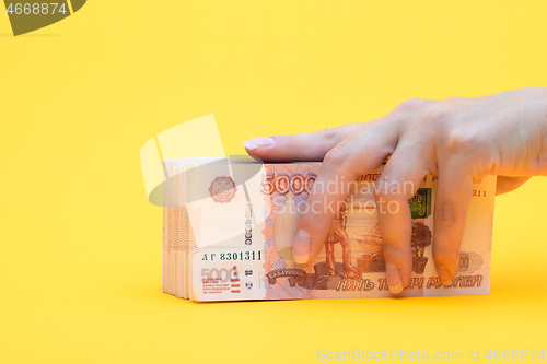 Image of Hand covered a pack of five thousandth bills, yellow background