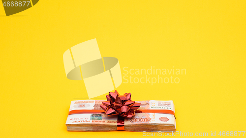 Image of A pack of five thousandth bills with red ribbons and a bow on a yellow background