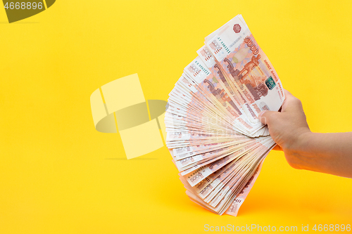 Image of Hand holds a fan from a pack of five thousandth Russian bills on a yellow background