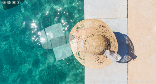 Image of Woman wearing big summer sun hat relaxing on pier by clear turquoise sea.