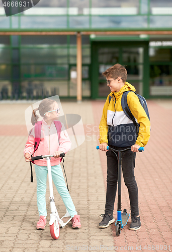 Image of happy school children with backpacks and scooters