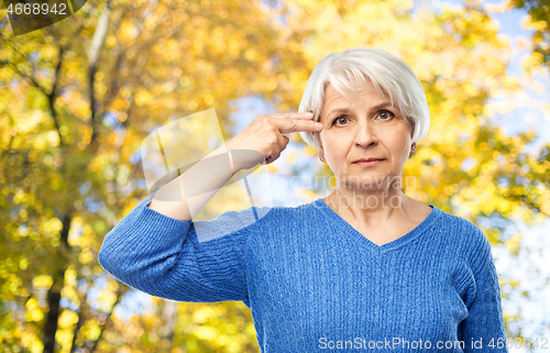 Image of old woman making finger gun gesture in autumn park