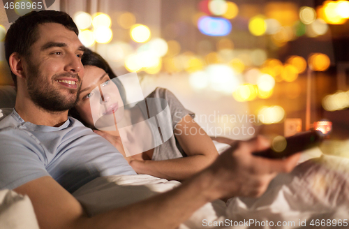 Image of happy couple watching tv in bed at night at home