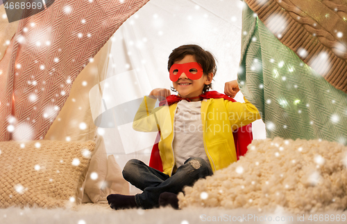 Image of happy boy in super hero cape in kids tent at home