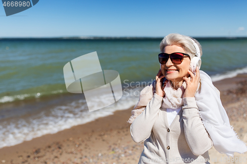 Image of old woman in headphones listens to music on beach