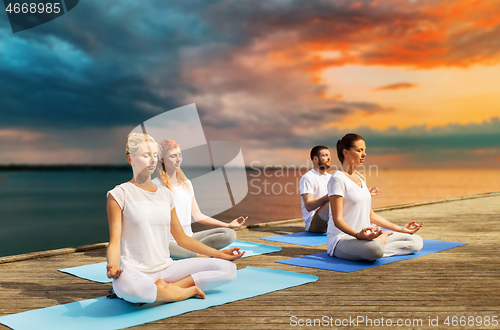 Image of people meditating in yoga lotus pose outdoors