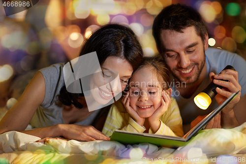 Image of happy family reading book in bed at night at home