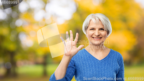 Image of smiling senior woman showing palm in autumn park