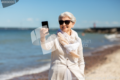 Image of senior woman taking selfie by smartphone on beach