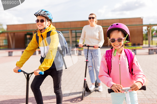 Image of happy school children with mother riding scooters