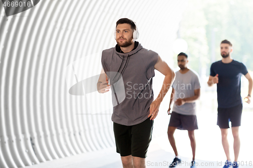 Image of male friends with headphones running outdoors