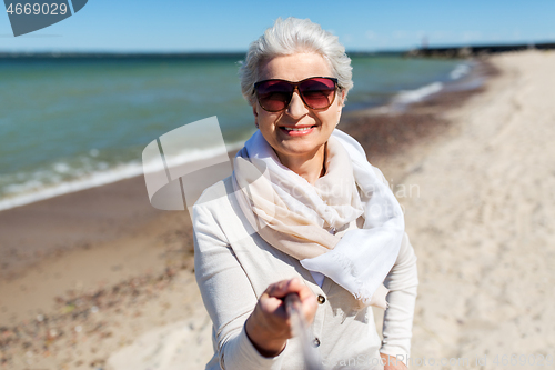 Image of old woman taking picture by selfie stick on beach