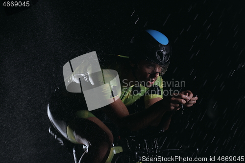 Image of triathlon athlete riding bike fast on rainy night