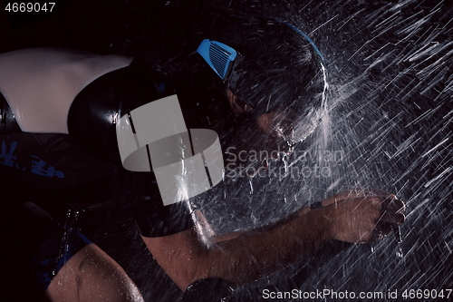 Image of triathlon athlete riding bike fast on rainy night