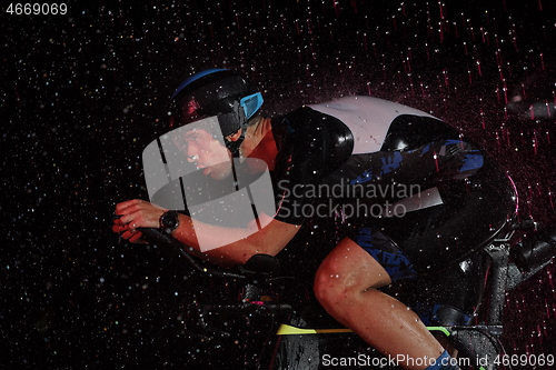 Image of triathlon athlete riding bike fast on rainy night